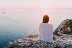 woman sitting on rock overlooking sunrise on body of water